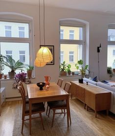 a living room filled with furniture and windows next to a wooden table surrounded by potted plants