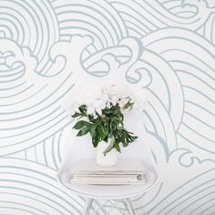 a vase with white flowers sitting on top of a stool in front of a wall