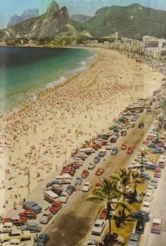 an aerial view of a crowded beach with cars parked on the sand and mountains in the background