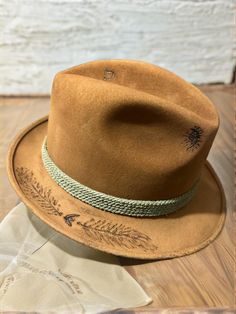 Title: Vintage Nitehawk Fedora in Suede with Braided Band Description: Embrace timeless style with this vintage Nitehawk Fedora, featuring a rich suede finish and a distinctive braided band accent. This hat showcases a weathered look that adds character, coupled with the classic fedora shape for a sleek profile. The interior label indicates it is made of quality velour, promising durability and comfort. Perfect for collectors and fashion enthusiasts alike, this hat combines functionality with an elegant aesthetic. Estimated Age: Likely from the 1970s or 1980s, given the design elements and branding style. Classic Brown Western Fedora, Southwestern Brown Fedora Hat, Brown Flat Brim Vintage Fedora, Vintage Handmade Brown Fedora, Brown Wide-brim Fedora With Feathers, Cow Boy, Timeless Style, Fedora, Cowboy Hats