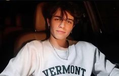 a young man wearing a vermont sweatshirt sitting in a car