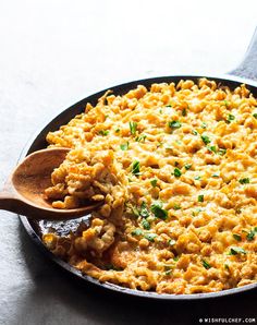 a skillet filled with macaroni and cheese on top of a table next to a wooden spoon