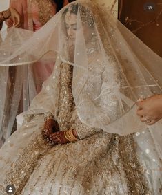 a woman in a white and gold wedding dress sitting on a chair with her veil draped over her head