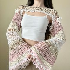 a woman is wearing a pink and white crochet shawl with open shoulders