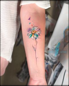 a woman's arm with a watercolor daisy tattoo on the left inner forearm