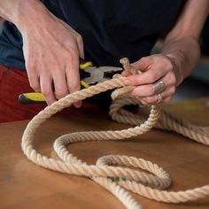 a person holding a pair of pliers and rope on top of a wooden table