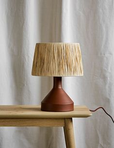 a lamp that is sitting on top of a wooden table next to a white curtain