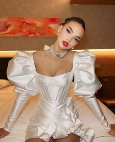 a woman sitting on top of a bed wearing a white dress