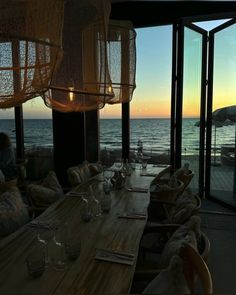 a dining room with large windows overlooking the ocean at sunset or sunrise, and people sitting in chairs looking out onto the water