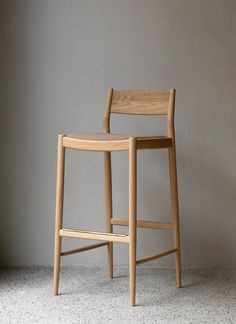 a wooden bar stool sitting on top of a white floor next to a gray wall