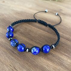 a blue beaded bracelet on a wooden table with silver beads and black cord around it