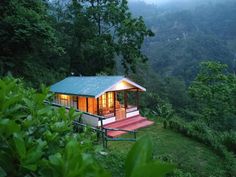 a small house sitting on top of a lush green hillside surrounded by trees and bushes