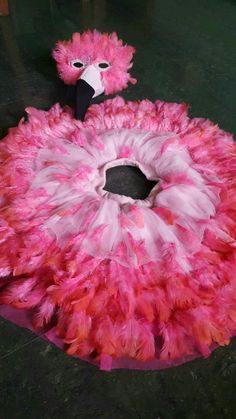 a pink and white feathered bird sitting on top of a black table next to a stuffed animal