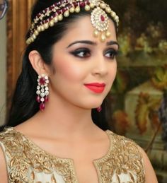 a woman wearing a head piece with pearls and jewels on her forehead, looking at the camera