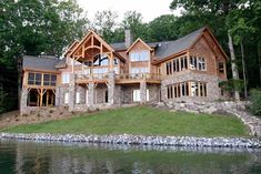 a large house sitting on top of a lush green hillside next to a body of water