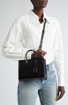 A compact Saint Laurent bag in smooth calfskin leather makes for a look that's as luxe as it is timeless. Featuring classic touches like the compression snap-straps that allow you to expand the capacity, as well as a leather-encased padlock and rolled top handles, the Sac de Jour is the last word in perennial style. Open top Top carry handles; adjustable shoulder strap Removable padlock with leather case; key fob snaps into interior of bag for storage Structured silhouette with flat base and pro Ysl Classic Bag, Sac Du Jour Saint Laurent Outfit, Wishes Board, Saint Laurent Outfit, Ysl Outfit, Timeless Handbags, Build Wardrobe, Luxury Wishlist, Cozy Streetwear