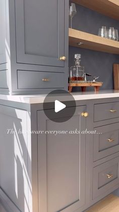 a kitchen with gray cabinets and white counter tops in the center is an open shelf that has wine glasses on it