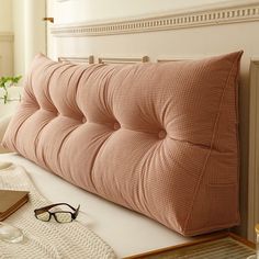 a pink pillow sitting on top of a bed next to a pair of reading glasses