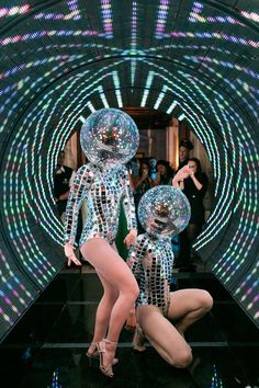 two women in bodysuits with disco balls on their heads and legs, standing next to each other