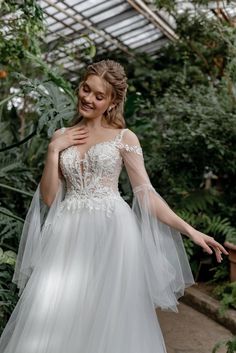 a woman in a white wedding dress is walking through the greenhouse with her arms outstretched