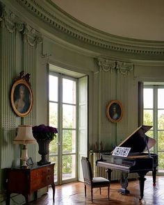 a grand piano sitting in the corner of a room with two large windows and paintings on the wall