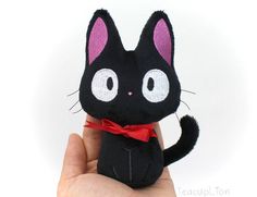 a hand holding a small black cat with pink eyes and a red bow around its neck