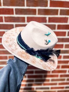 This beige bent brim hat features a stunning hand burned floral design, giving it a unique and rustic feel. The addition of black and turquoise accessories adds a touch of sophistication and style to this classic cowgirl hat. Whether you're heading to the rodeo or simply wanting to add a statement piece to your outfit, this hat is the perfect choice. Made with high-quality materials and expert craftsmanship, this hat is durable and built to last. Complete your Western look with this striking Wild West Bent Brim Hat. Bohemian Cream Fedora Sun Hat, Cream Bohemian Fedora Sun Hat, Bohemian Cream Fedora With Flat Brim, Cream Bohemian Brimmed Hat, Cream Bohemian Adjustable Hat, Cream Brimmed Fedora For Festival, Bohemian Wide Brim Cream Fedora, Bohemian Cream Wide Brim Fedora, Spring Festival Cream Fedora