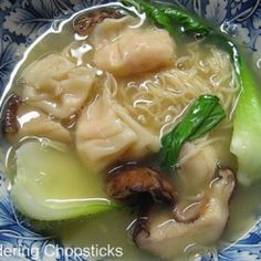 a blue and white bowl filled with dumplings, cucumbers and mushrooms in broth