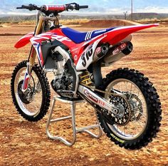 a red, white and blue dirt bike parked on top of a stand in the desert