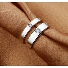 two white gold wedding rings with diamonds on top of each other, sitting on a brown cloth