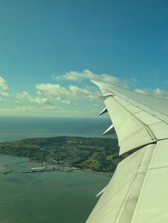 the wing of an airplane as it flies over some water and land in the background