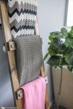 a wooden chair with two blankets on it and a potted plant in the background