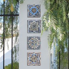 three blue and white tiles are hanging on the wall next to a plant in front of a gate