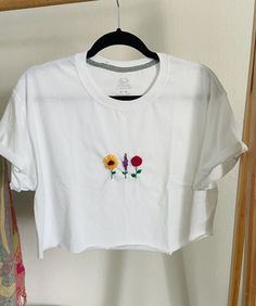 Thank you for your interest! This item is a hand embroidered cropped tee. The sleeves are tiled and stitched and the bottom is a raw edge. The design is 3 different flowers a sun flower, a rose and a lavender branch.  -Men's T-shirt  -size men's M  -Fruit of the loom  -hand embroidred  colors: green, brown, yellow, red, purple White Tee Embroidery, Spring Cotton Crop Top With Floral Embroidery, Spring Floral Embroidery Cotton Crop Top, Casual Cotton Crop Top With Floral Embroidery, Casual Embroidered Cropped Top, White Embroidered Cotton Crop Top, Casual Embroidered Crop Top For Summer, Casual Floral Embroidery Crop Top For Spring, Floral Embroidered Summer T-shirt