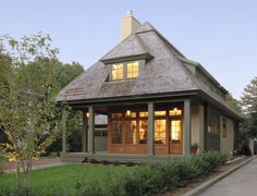 a small house with a porch and covered in shingles on the roof, surrounded by greenery