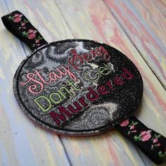 a black and pink hand mirror with words on it sitting on a wooden table next to a pair of scissors