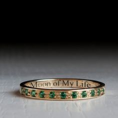 a close up of a ring with green stones on the bottom and words written in gold