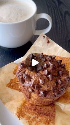 a cup of coffee sitting next to a doughnut on top of a piece of wax paper