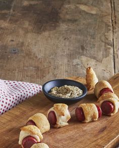 hotdogs wrapped in bread on a cutting board next to a bowl of dip