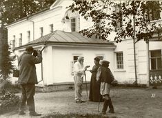 an old black and white photo of people standing in front of a house with a camera