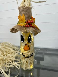 a glass bottle with a scarecrow face on it sitting on a table next to shredded hay