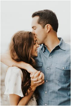 a man and woman kissing each other while standing next to each other in front of the ocean