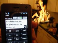 a person holding up a cell phone in front of a fire filled kitchen with white cabinets