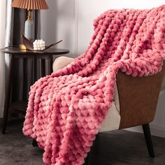 a pink blanket sitting on top of a brown chair next to a lamp and table