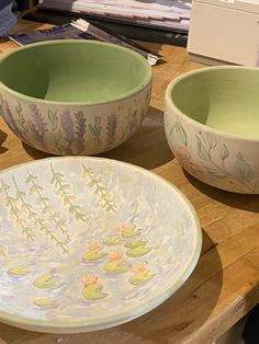 two bowls sitting on top of a wooden table next to each other with flowers painted on them