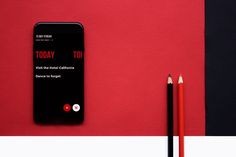 a cell phone sitting on top of a table next to two pencils and a red wall