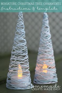 two small white christmas trees sitting on top of a table with lit candles in them