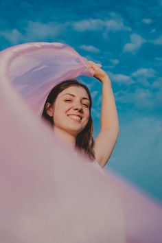 a woman is smiling and holding her pink scarf over her head while looking up into the sky