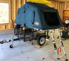 a trailer with a tent attached to it in a room under construction, next to a surfboard rack