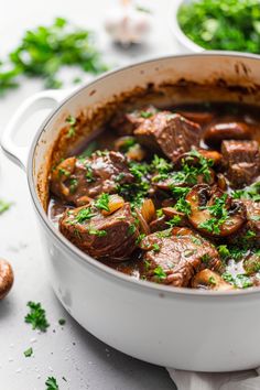 a pot filled with stew and vegetables on top of a white countertop next to other dishes